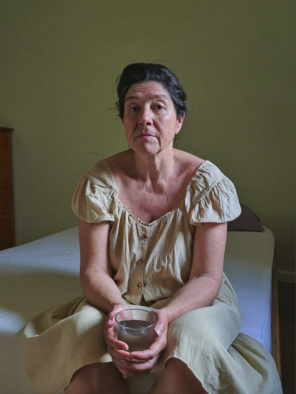 Vrouw zit ’s ochtends op de rand van haar bed met een glas water